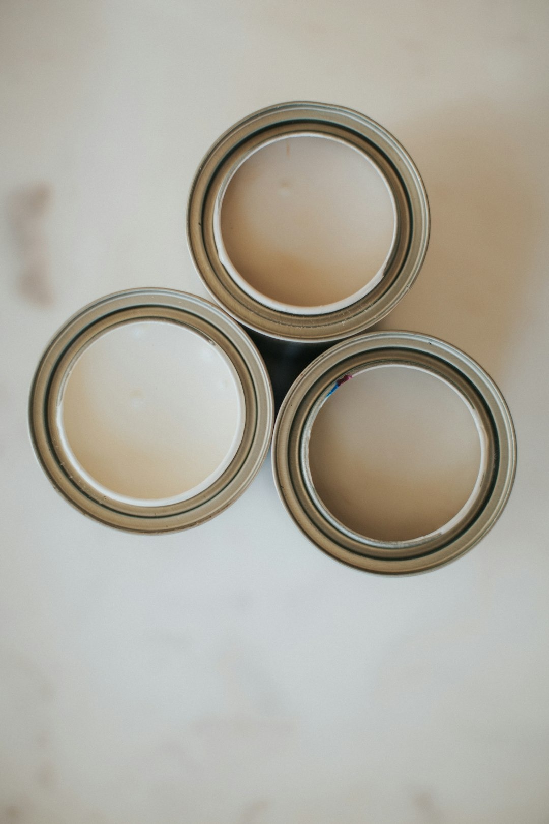 Three open cans of beige paint arranged on a surface.