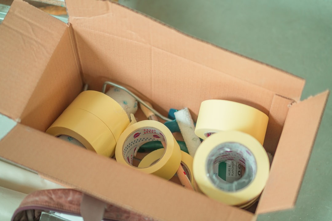 Cardboard box filled with yellow masking tape and paint rollers.